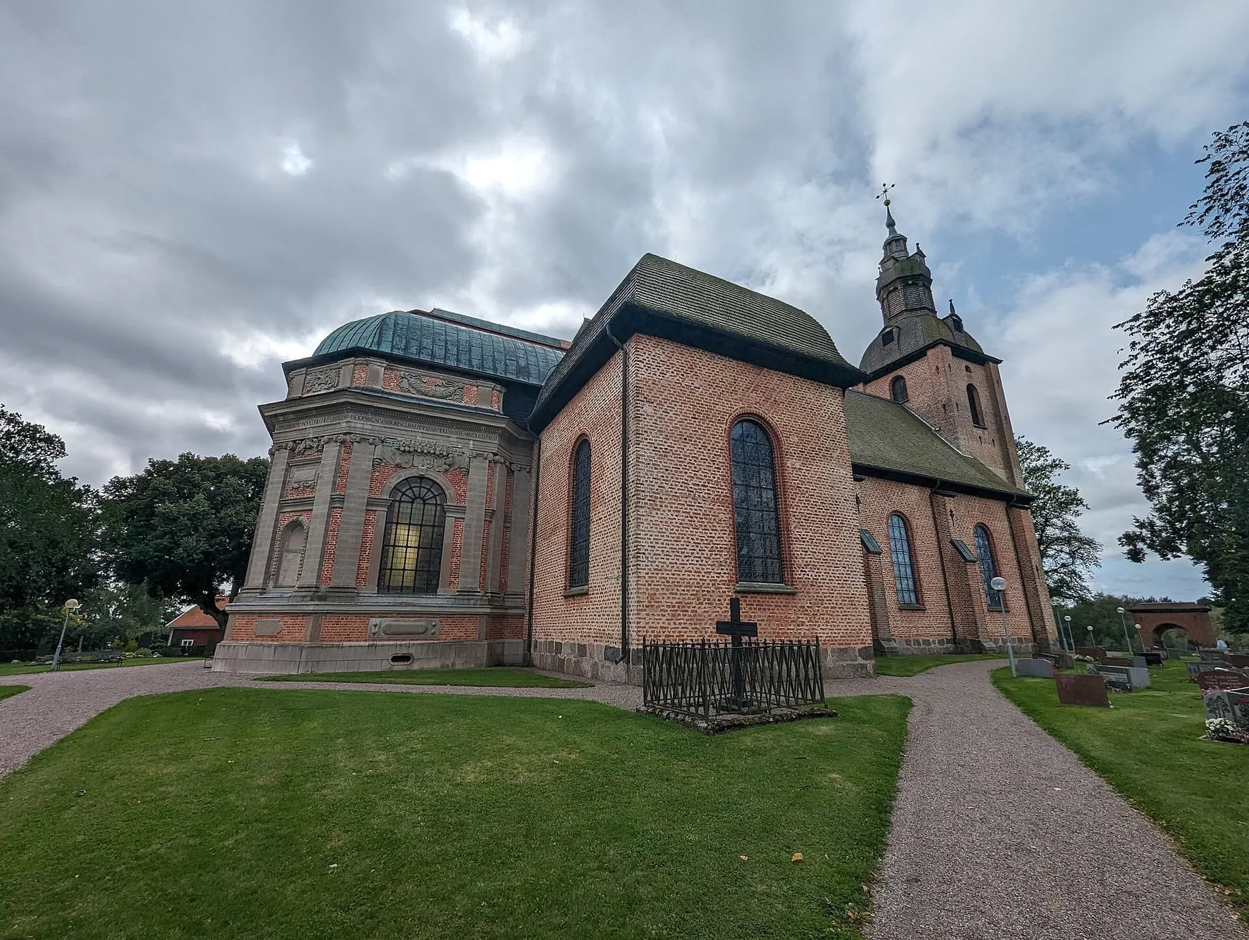 Askersunds landskyrka, en stor tegelkyrka med torn och ett kupoltäckt gravkor, omgiven av gräsmatta och grusgångar.